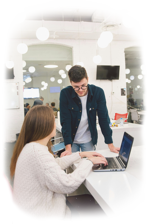 A young man helping a woman sitting at a computer